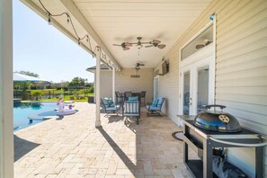 Eine überdachte Terrasse mit Gartenmöbeln, einem Grill und einem Swimmingpool.