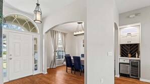 Um quarto espaçoso com piso de madeira, paredes brancas, área de refeições com cadeiras azuis e cozinha equipada com geladeira e armários.