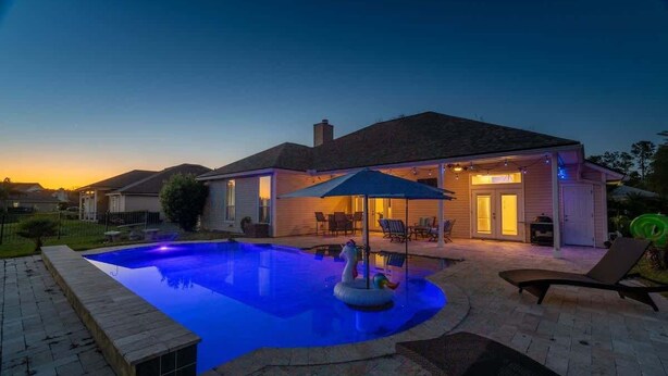 Piscina residencial com área de estar, um alpendre coberto e uma casa ao fundo.