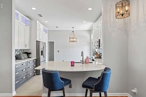 A modern kitchen with white cabinets, a central island with two chairs, a chandelier, and a built-in oven. - Peacock Shores | Team Joseph Ellen (Jacksonville)