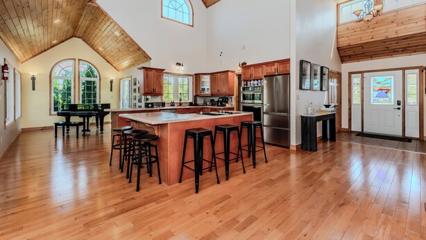A spacious kitchen with a large island, wooden ceiling, and large windows.