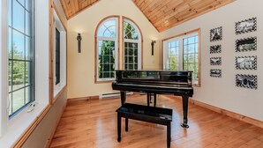 A spacious room with a grand piano, large arched windows, and wall-mounted picture frames.