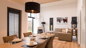 A modern dining area with a long table set for four, a sofa, and a floor lamp. - Ground floor bungalow for 4 persons (Herkingen)