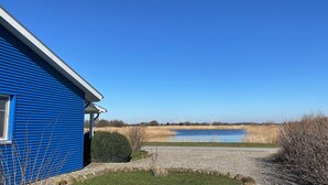 Un edificio azul con un camino de grava que conduce a una masa de agua, rodeado de aerogeneradores y vegetación.