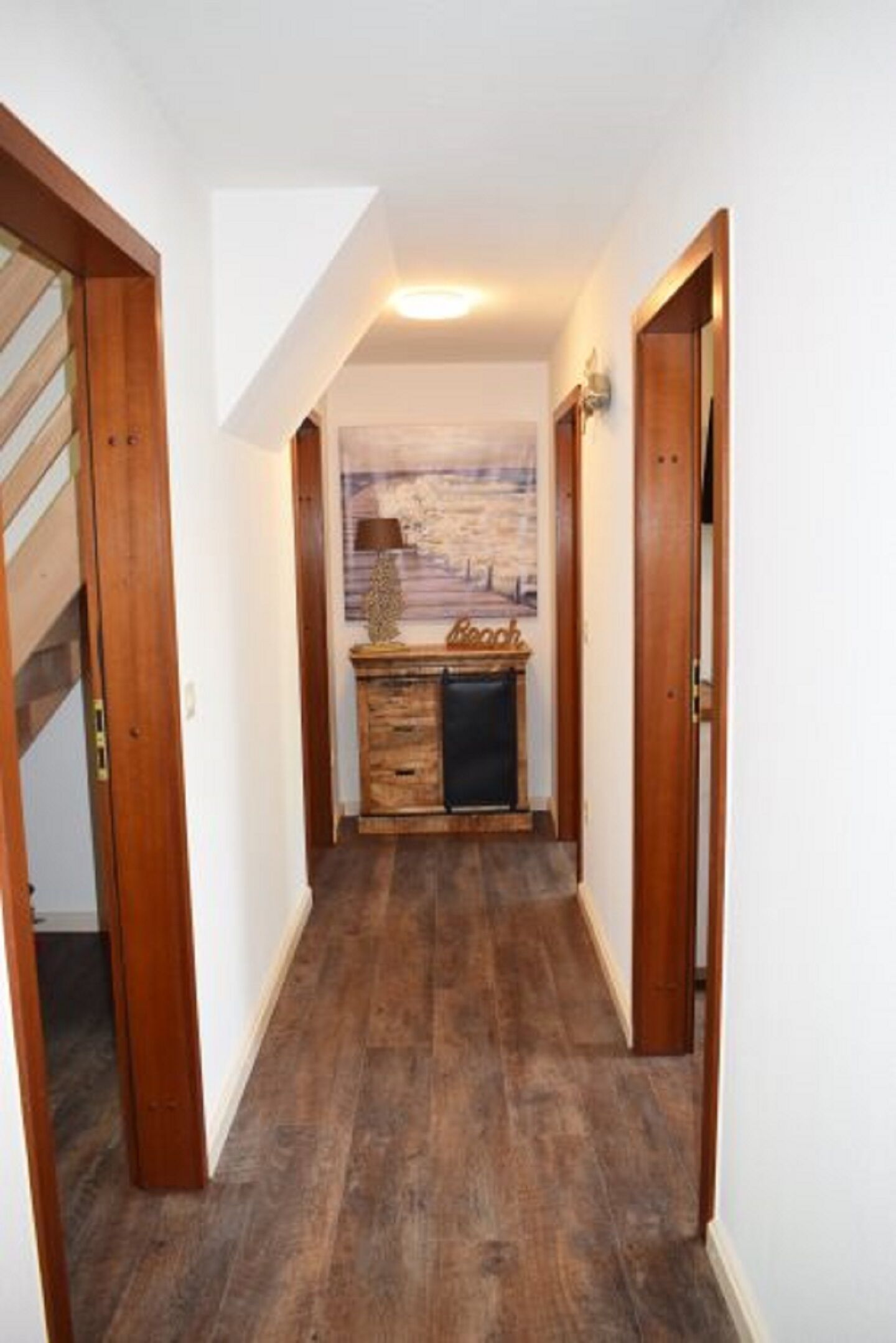 A hallway with wooden flooring, white walls, and a wooden door on the left.