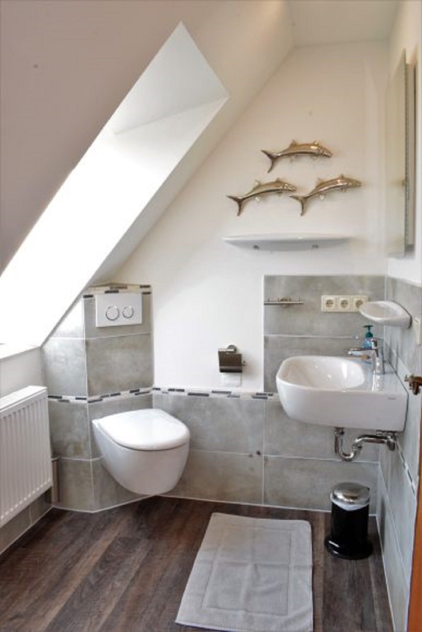 A modern bathroom with a sloped ceiling, a toilet, a sink, and decorative fish wall art.