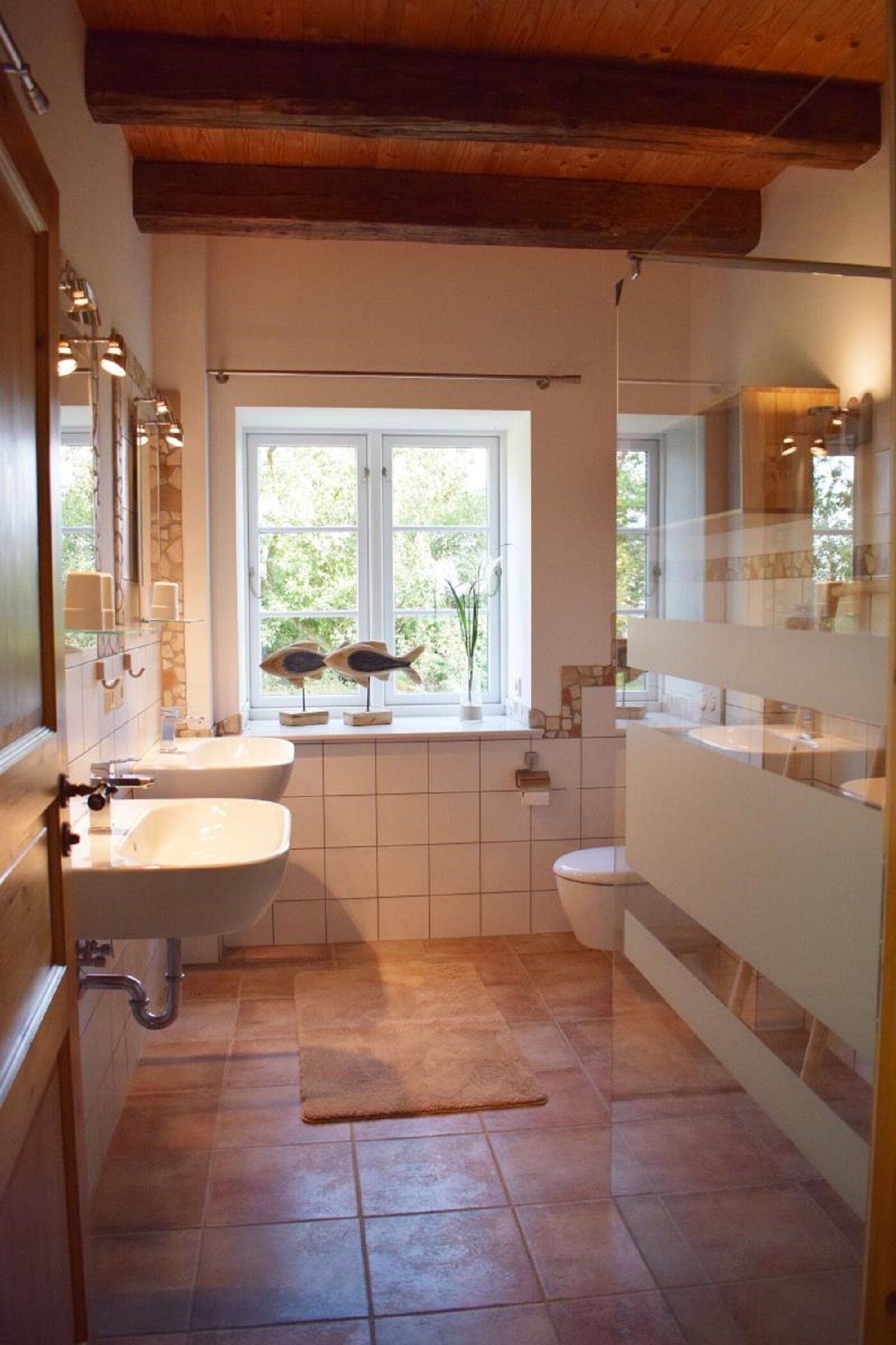 Et badeværelse med stort vindue, vask, toilet og spejl.