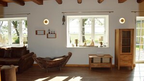 A cozy living room with a wooden ceiling, a large window with a view of greenery, a wicker sofa, a small table, and a cabinet. - "Experience Tranquility and Adventure in Ole Hof Risum-Lindholm!" (Risum-Lindholm)