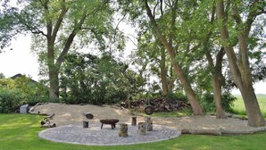 A circular stone patio with a fire pit, surrounded by a grassy area and trees. - "Experience Tranquility and Adventure in Ole Hof Risum-Lindholm!" (Risum-Lindholm)