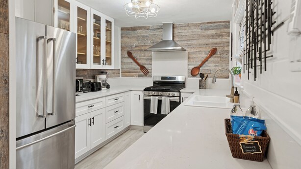 Una cocina moderna con electrodomésticos de acero inoxidable, armarios blancos y un panel posterior de madera.