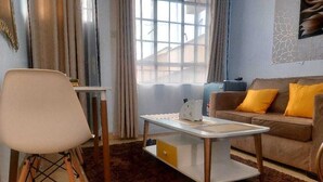 Un salon moderne avec une table basse blanche, un canapé marron agrémenté de coussins jaunes et un fauteuil blanc.