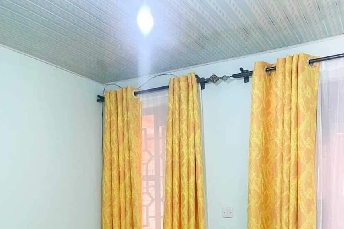 Ein Zimmer mit einem grünen Sofa, zwei kleinen weißen Tischen und gelb gemusterten Vorhängen.