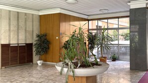 A spacious lobby with a marble floor, large potted plants, wooden paneling, and large windows. - Sandrine - your comfy stay (Bologna)
