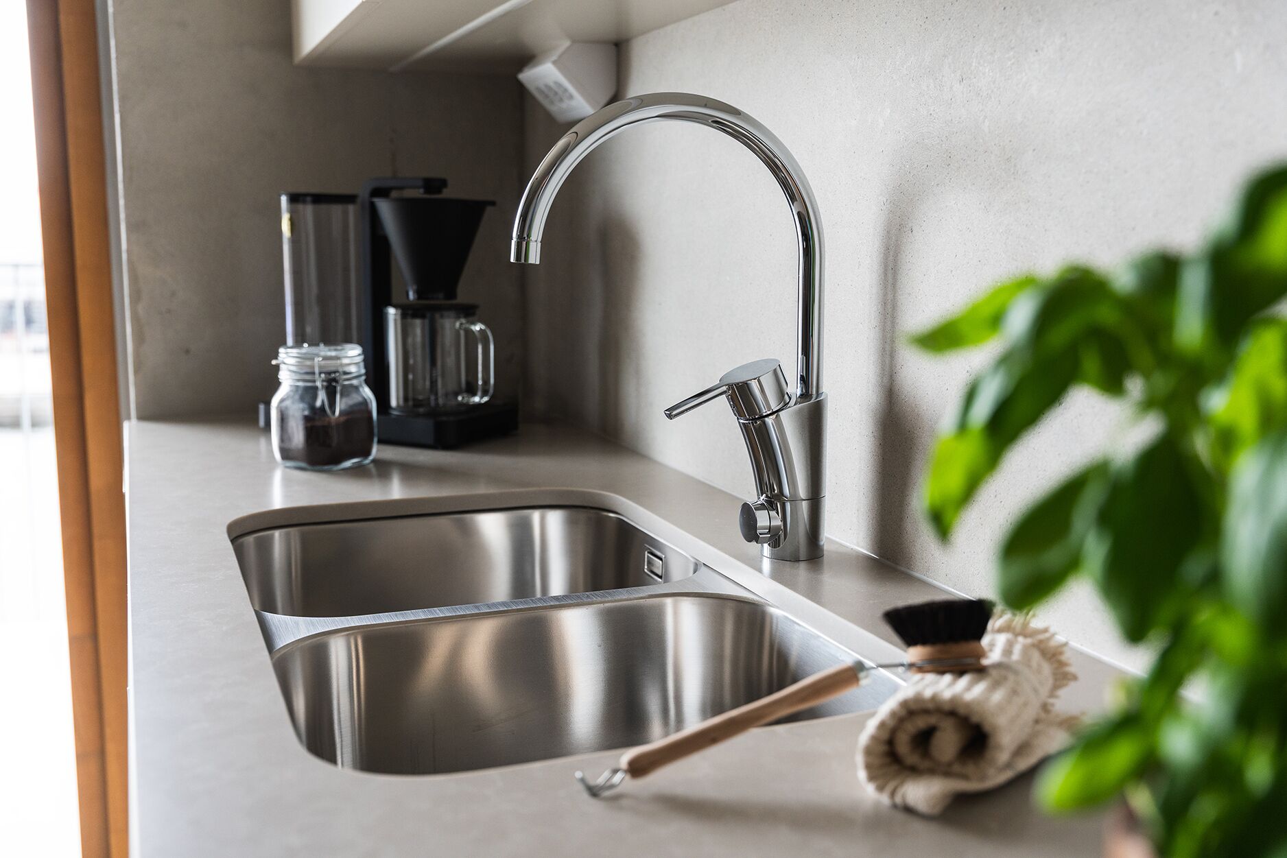 Una cocina moderna con un lavamanos de acero inoxidable, una cafetera y una toalla enrollada sobre la encimera.