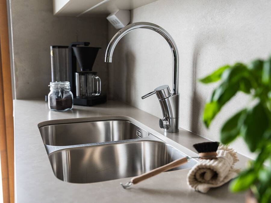 Una cocina moderna con un lavamanos de acero inoxidable, una cafetera y una toalla enrollada sobre la encimera.