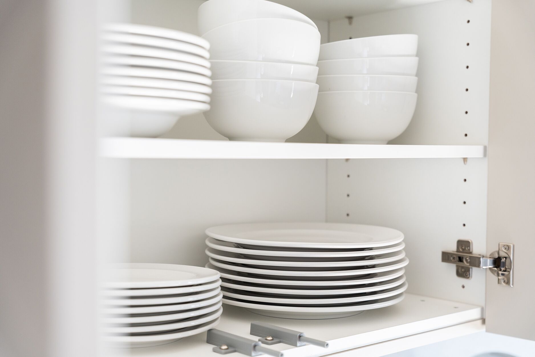 A kitchen with white cabinets and shelves holding white plates and bowls.