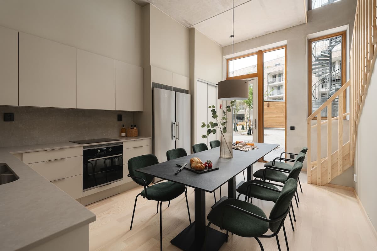 A modern kitchen with a dining area, featuring a large table, chairs, and a view of the outside.