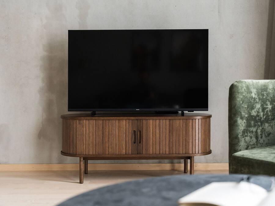 A modern living room with a flat-screen TV on a wooden cabinet, a green upholstered chair, and a book on a table.