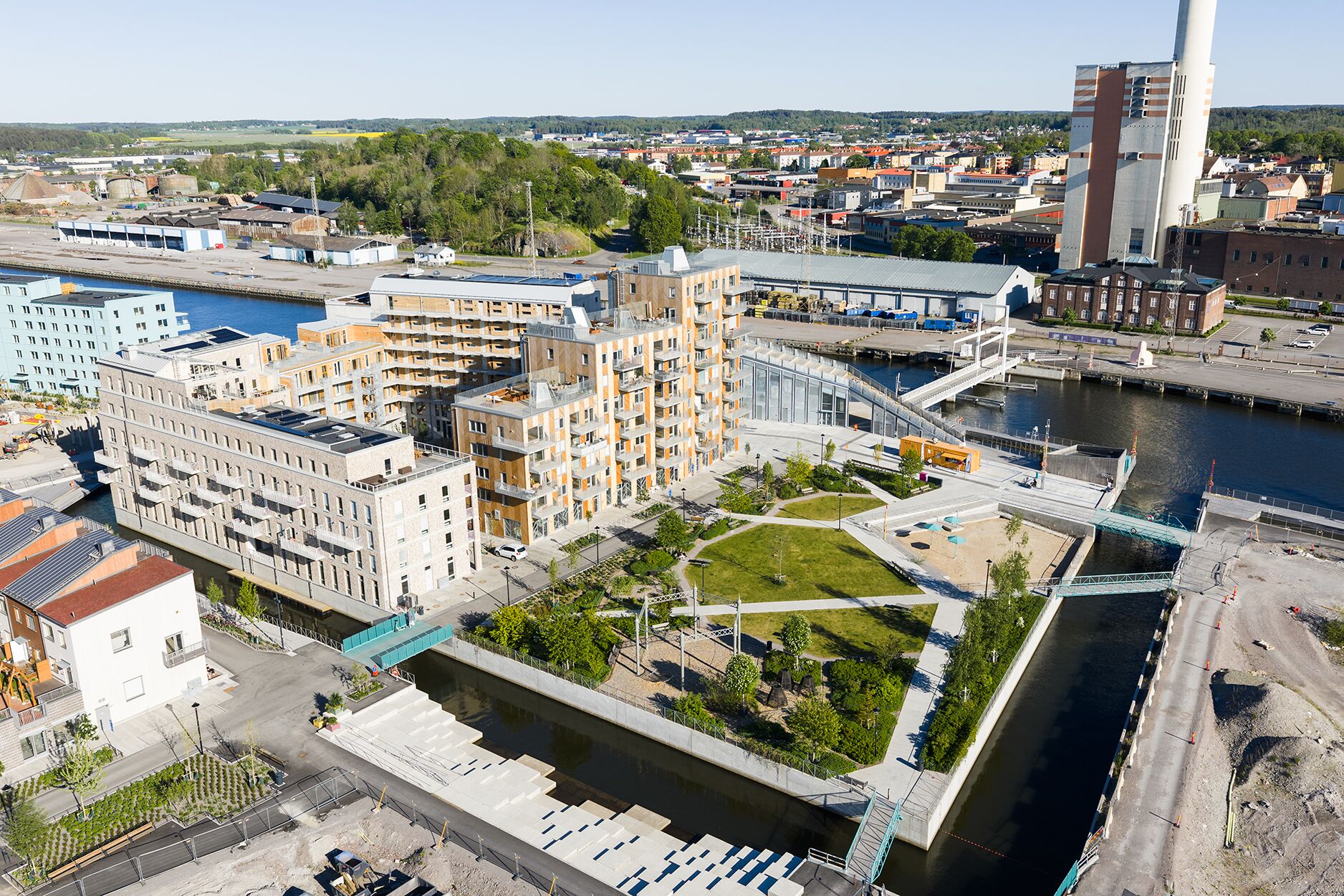 A high-rise building with multiple floors, a river in the foreground, and a bridge connecting to another area.