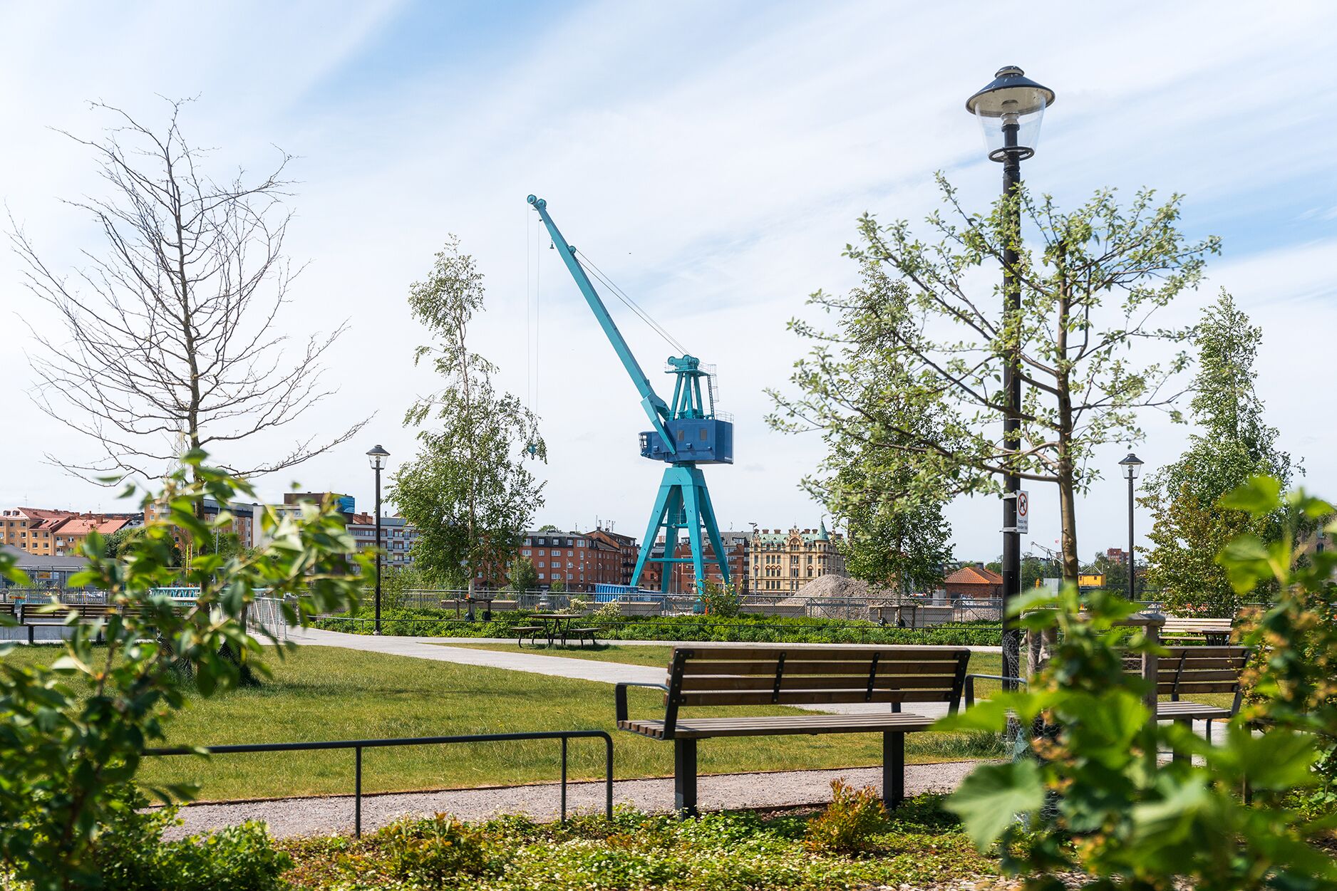 En park med bänkar, en gångstig och en stor blå kran i bakgrunden.