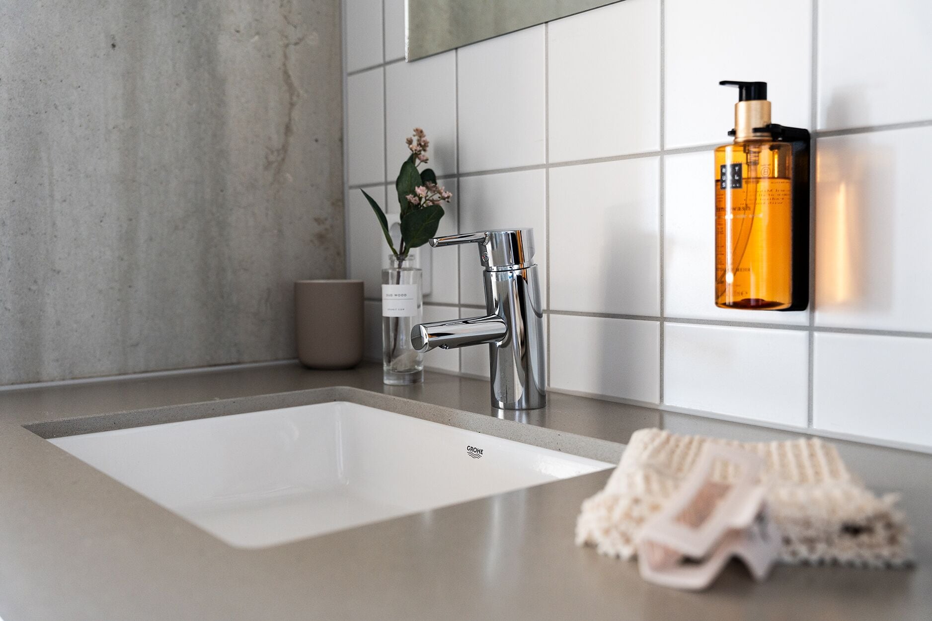 Un baño moderno con un grifo cromado, un lavabo blanco y una botella de jabón en la pared.