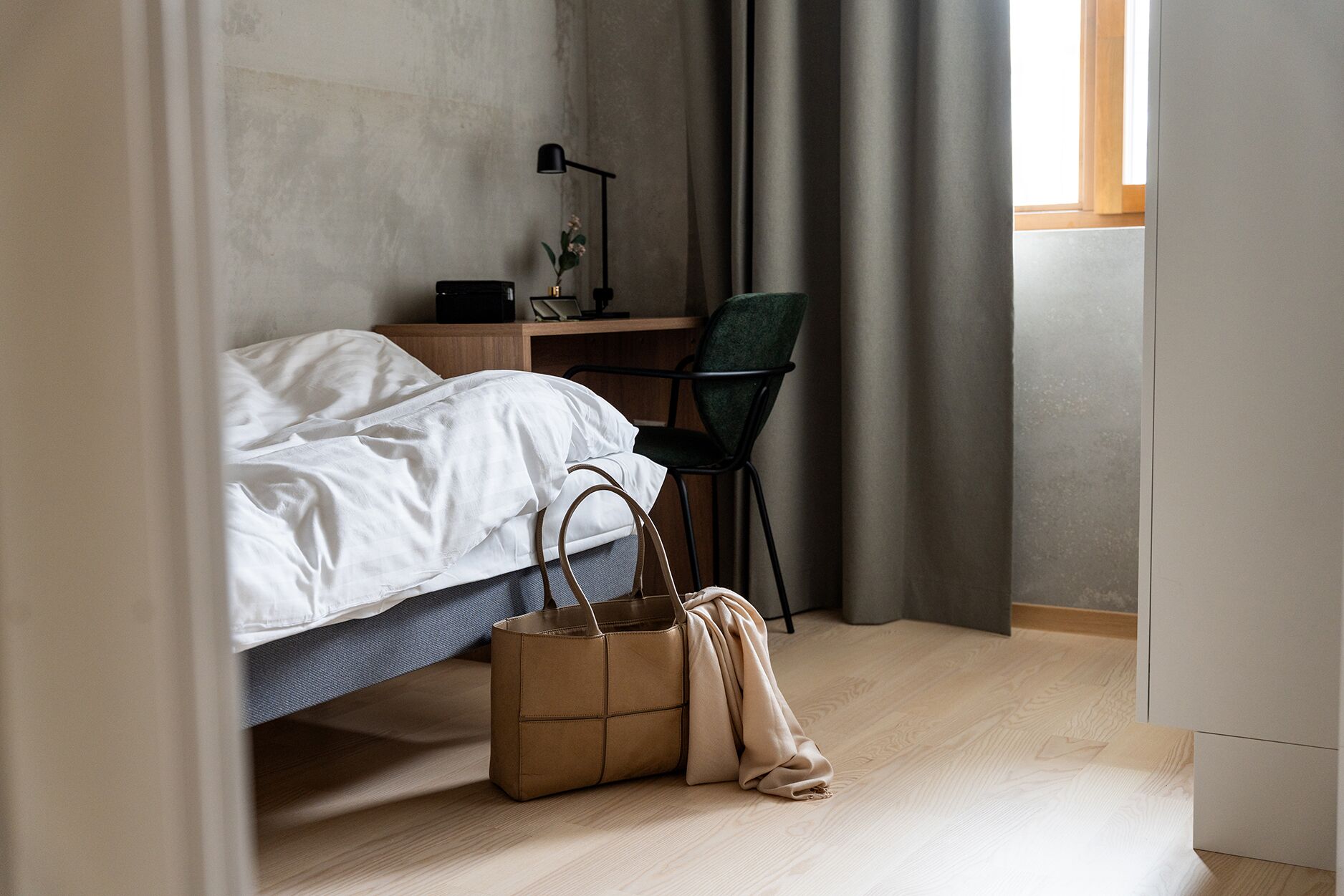 Un dormitorio con una cama, un escritorio, una silla y una bolsa en el suelo.