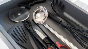 Un cajón con varios utensilios de cocina, incluyendo un par de tijeras, una cuchara para servir y varias espátulas.