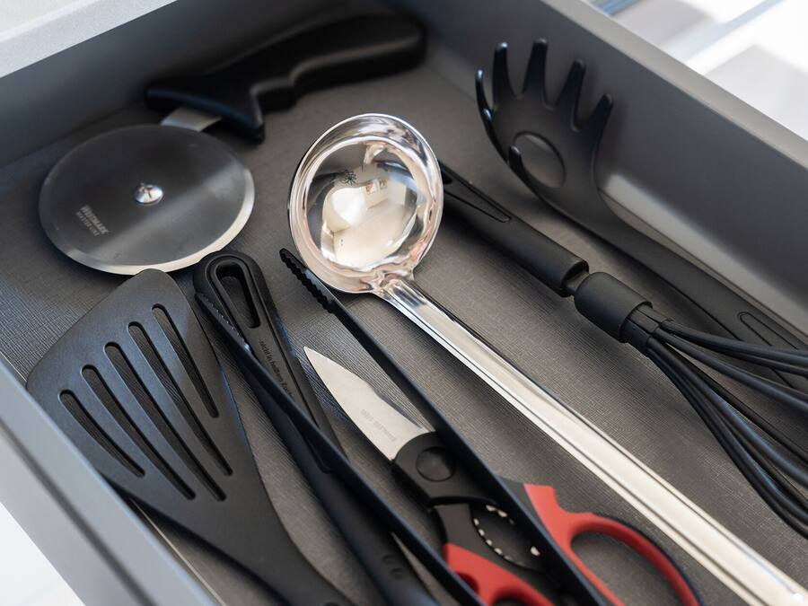 Un cajón con varios utensilios de cocina, incluyendo un par de tijeras, una cuchara para servir y varias espátulas.
