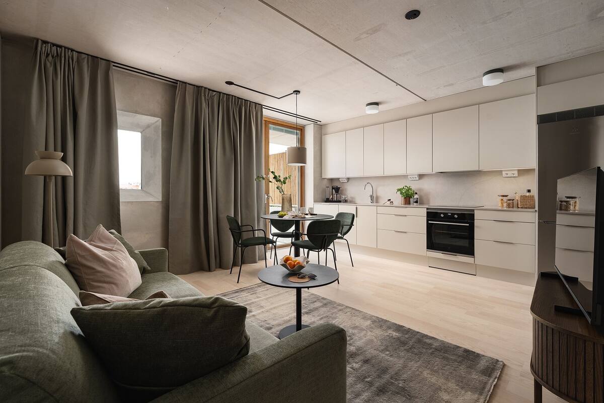A modern living room with a sofa, a dining table with chairs, and a kitchen area with cabinets and appliances.