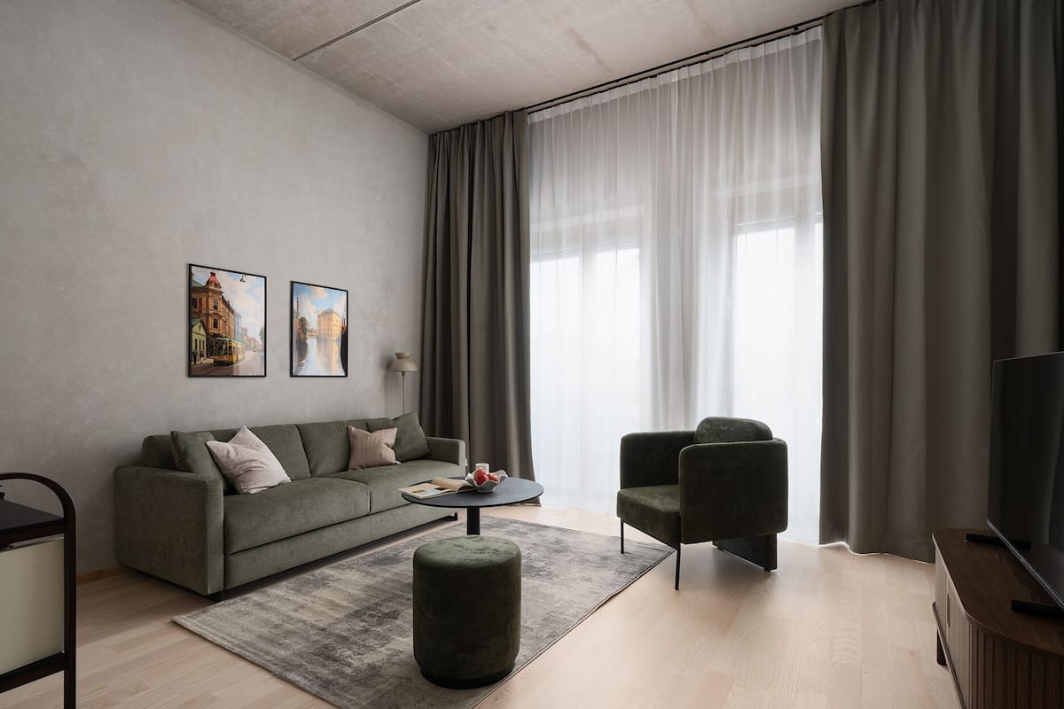 A modern living room with a grey sofa, two armchairs, a coffee table, and a TV on a wooden stand. There are two framed pictures on the wall and a lamp beside the sofa.