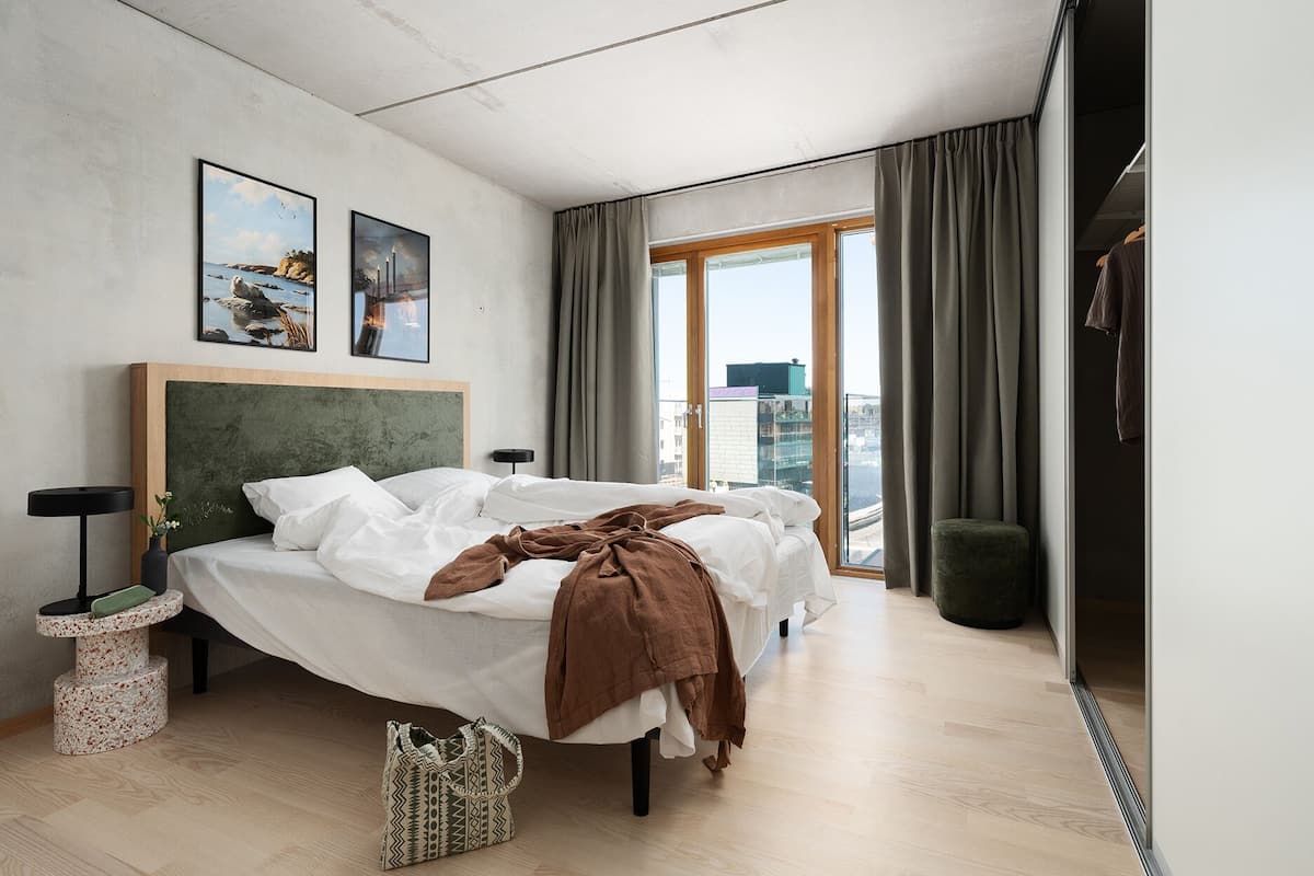 A modern hotel room with a large bed, a view of the city, and a cityscape painting on the wall.