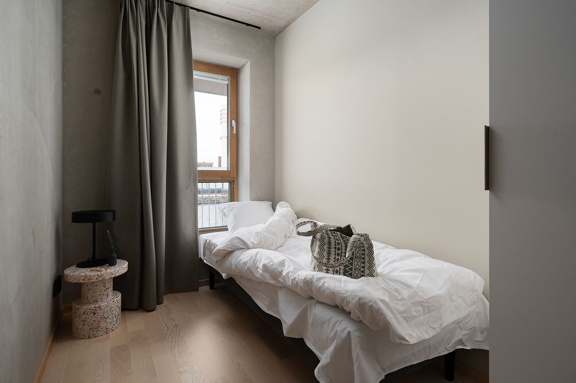 Un dormitorio pequeño y minimalista con una cama individual, un ventanal y una mesita de noche.