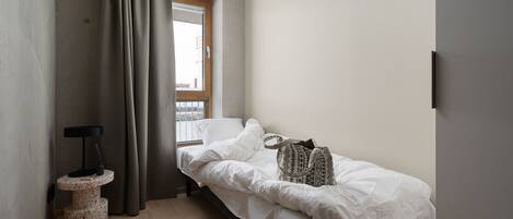 Un dormitorio pequeño y minimalista con una cama individual, un ventanal y una mesita de noche.