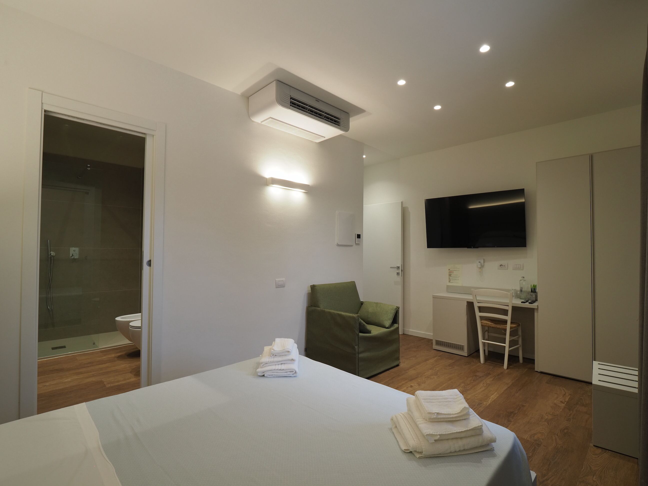 A hotel room with a bed, a desk, a chair, a TV, and a shower area.