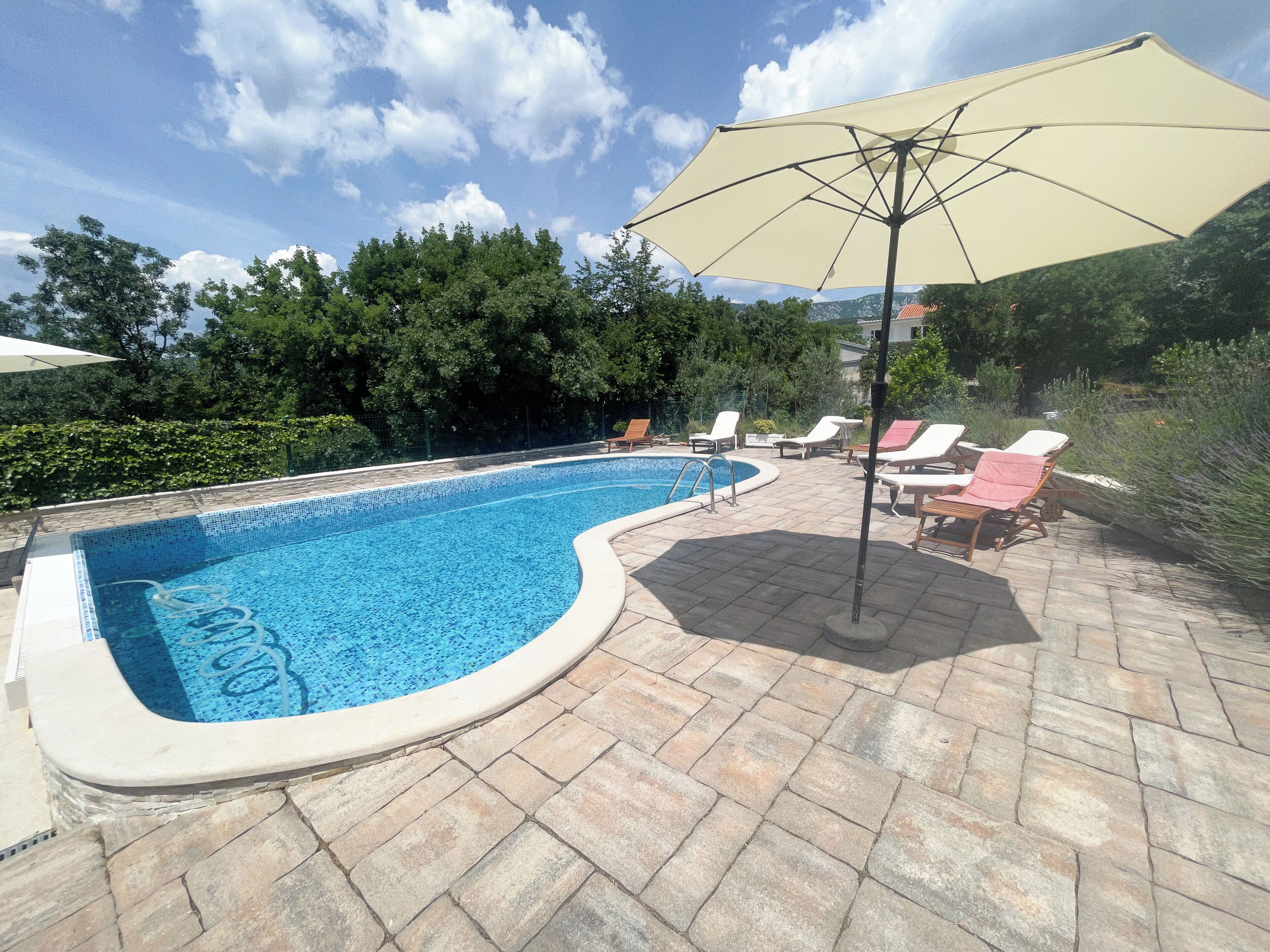 Una piscina de borde curvo, rodeada de sillas de descanso y una sombrilla.