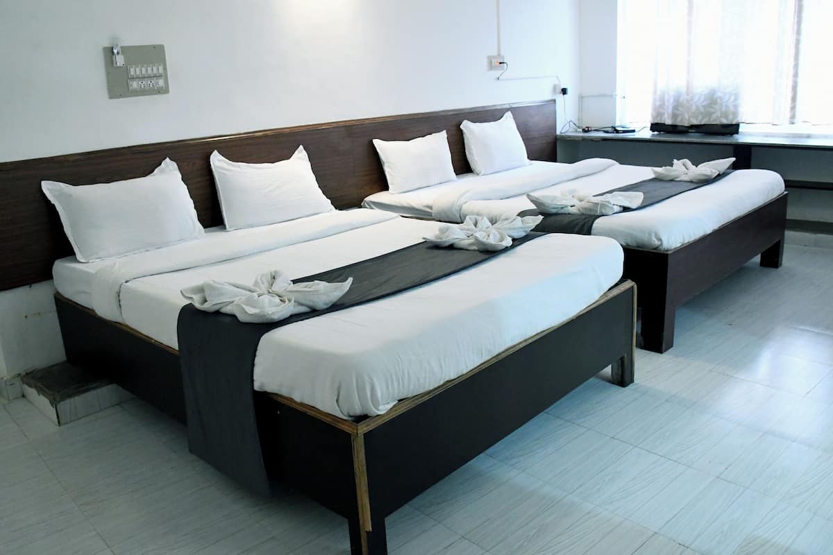 Una habitación de hotel con tres camas, una ventana con cortinas y un enchufe en la pared.