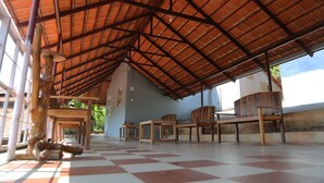 Un espace extérieur abrité, doté d’un sol à carreaux, de chaises en bois et, en arrière-plan, d’un bâtiment bleu.