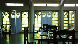 Un restaurant doté de grandes fenêtres ornées de vitraux, de tables et de chaises en bois, et d’un intérieur épuré et moderne.