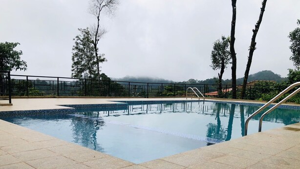 Une piscine avec une terrasse carrelée, des garde-corps en métal et des arbres en arrière-plan.