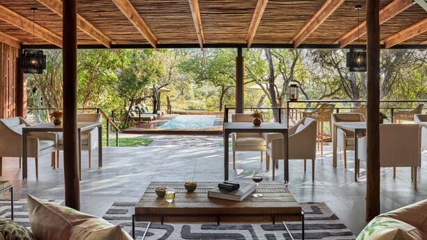 A covered outdoor seating area with a pool, lounge chairs, and a dining table. - Taj Bush Lodge (Hoedspruit)