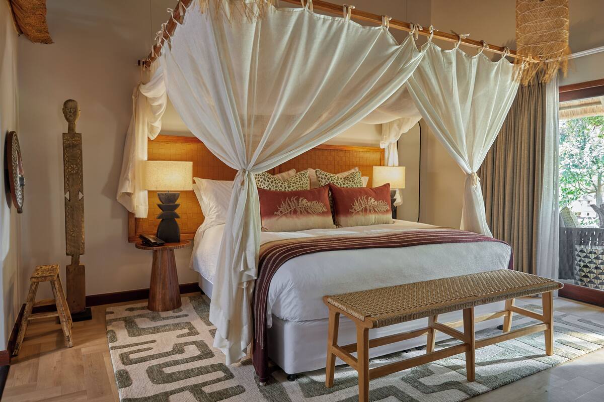 A bedroom with a canopy bed, bedside lamps, a wooden bench, and a patterned rug.