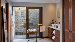 A modern bathroom with a stone wall, a sink with a mirror, and a towel rack. - Taj Bush Lodge (Hoedspruit)