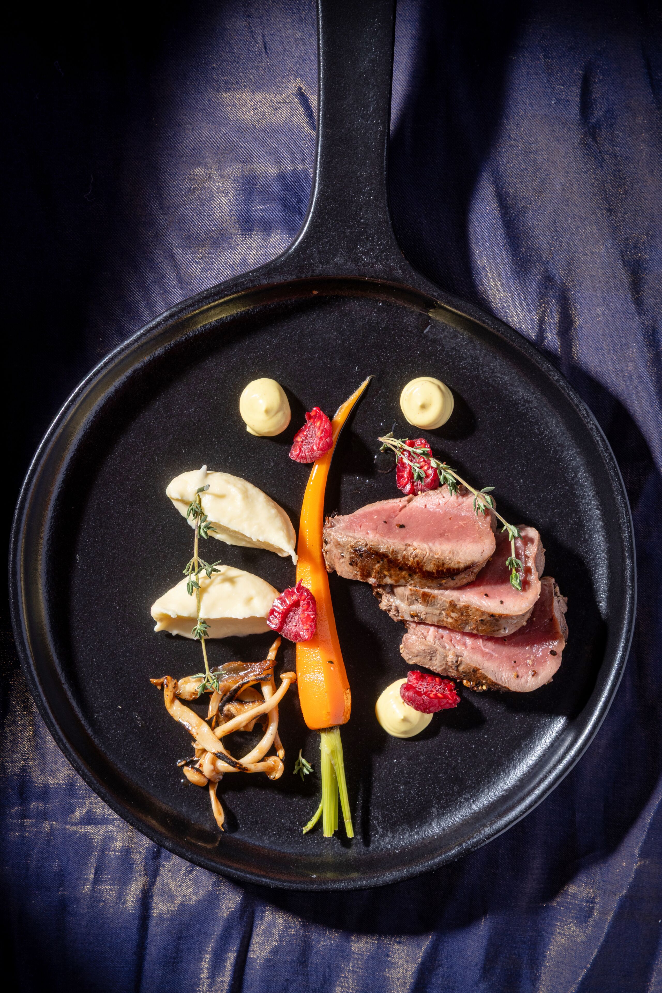 Una sartén con comida, incluyendo carne y verduras, sobre una superficie oscura.