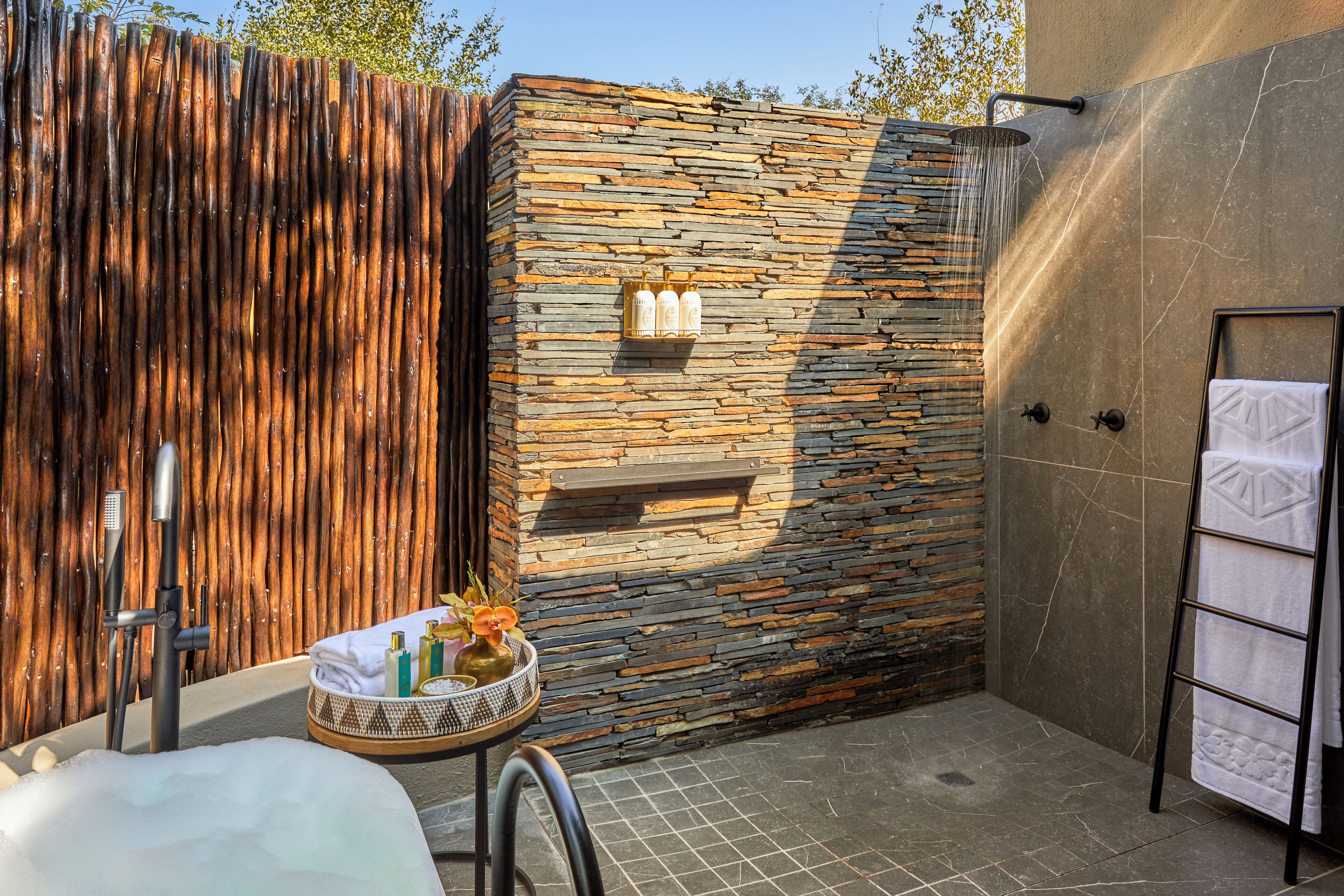 Un mur en pierre avec une douche, un porte-serviettes et une petite table sur laquelle sont posés des articles de toilette.