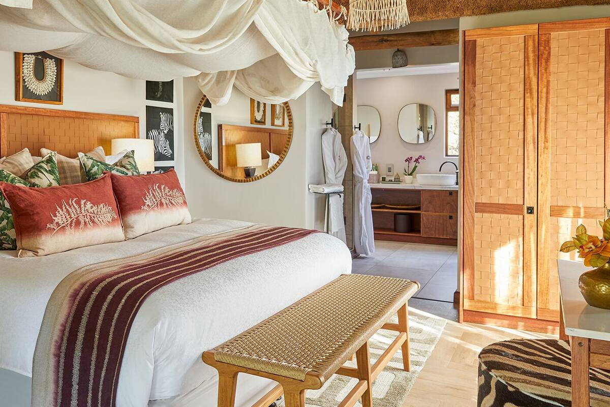 A well-appointed bedroom with a large bed, bedside tables, a bench, and a bathroom visible in the background.