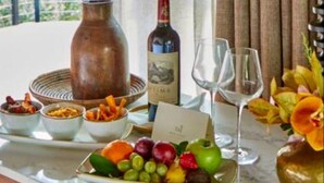 A table with a bottle, glasses, fruit, and a vase. - Taj Bush Lodge (Hoedspruit)