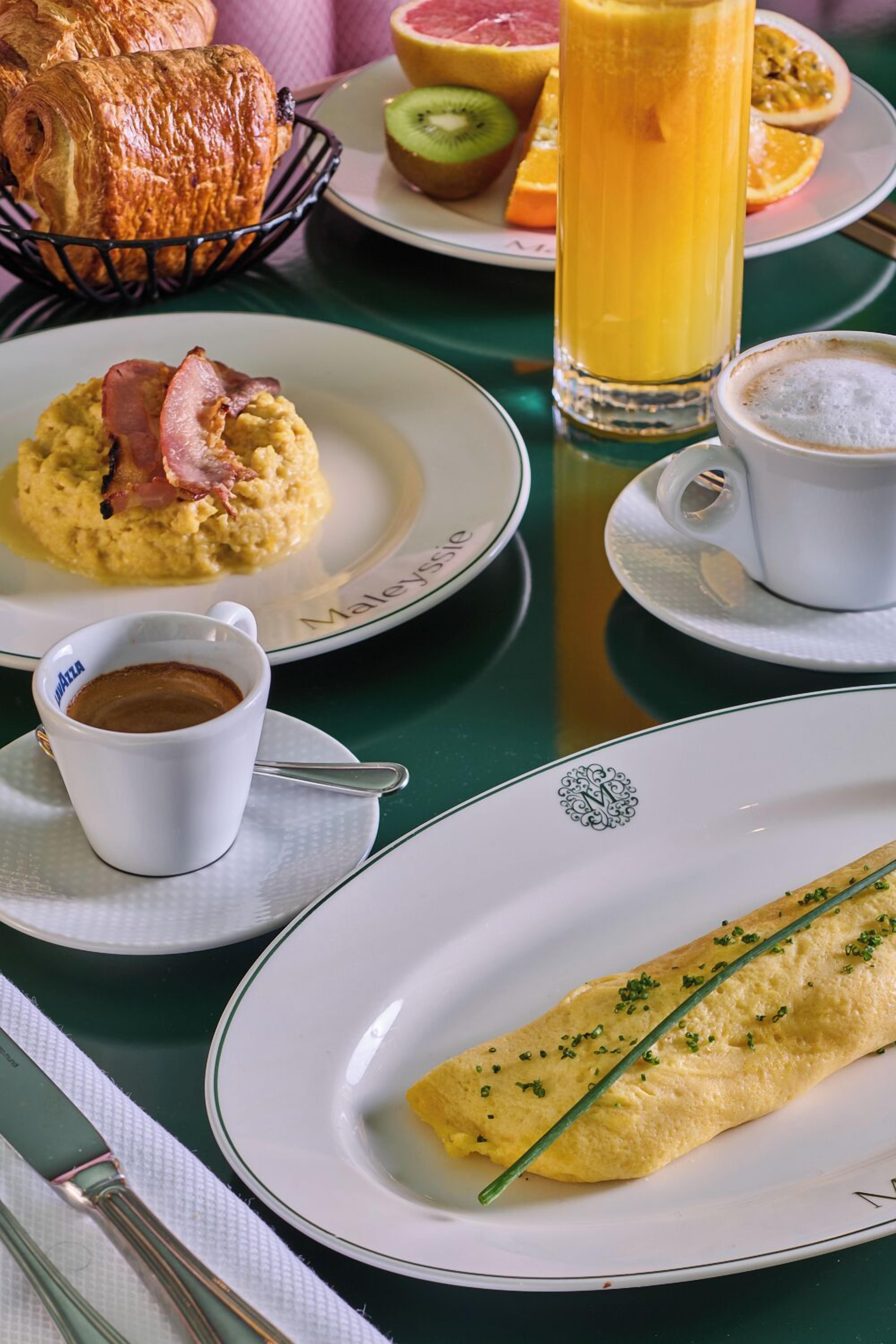 A breakfast table with croissants, scrambled eggs with bacon, a glass of orange juice, a cup of coffee, and an omelette.