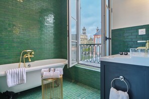 Ein Badezimmer mit einer Badewanne, einem Fenster mit Blick auf Gebäude und einem Waschbecken mit Handtuchhalter.