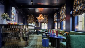 Een bar met een gebogen toonbank, groene bekleding en versierde kroonluchters.