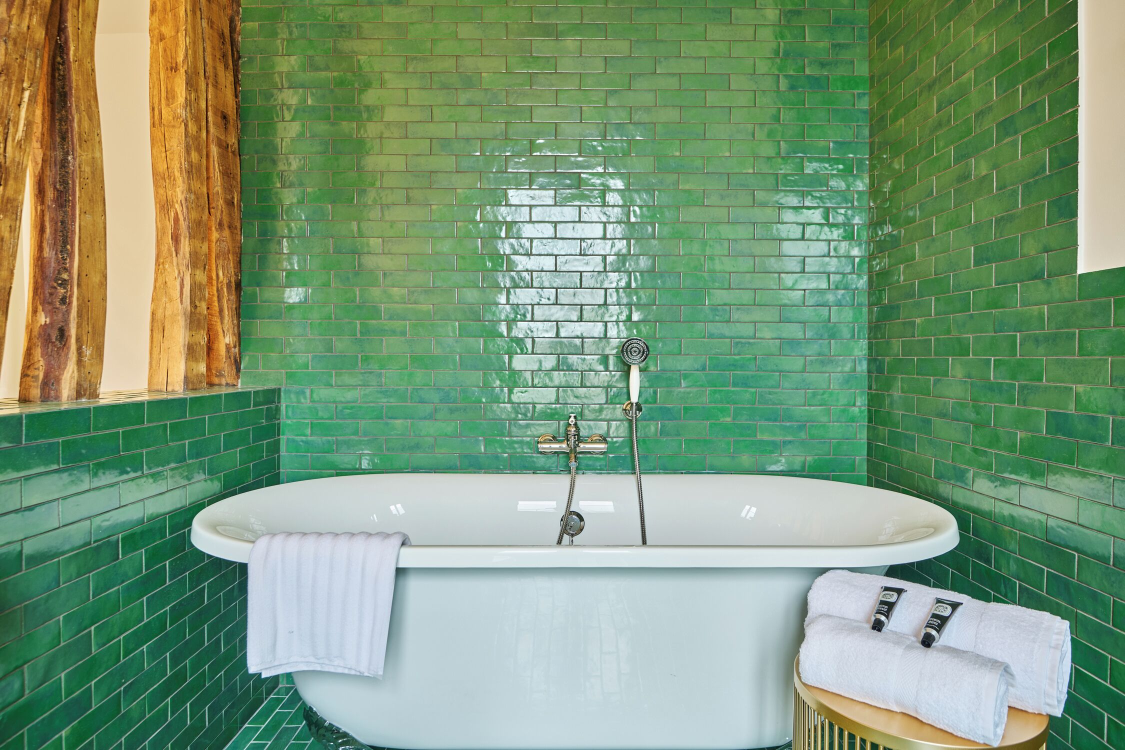 A bathroom with a freestanding bathtub, green-tiled walls, and a wooden vanity with a towel.